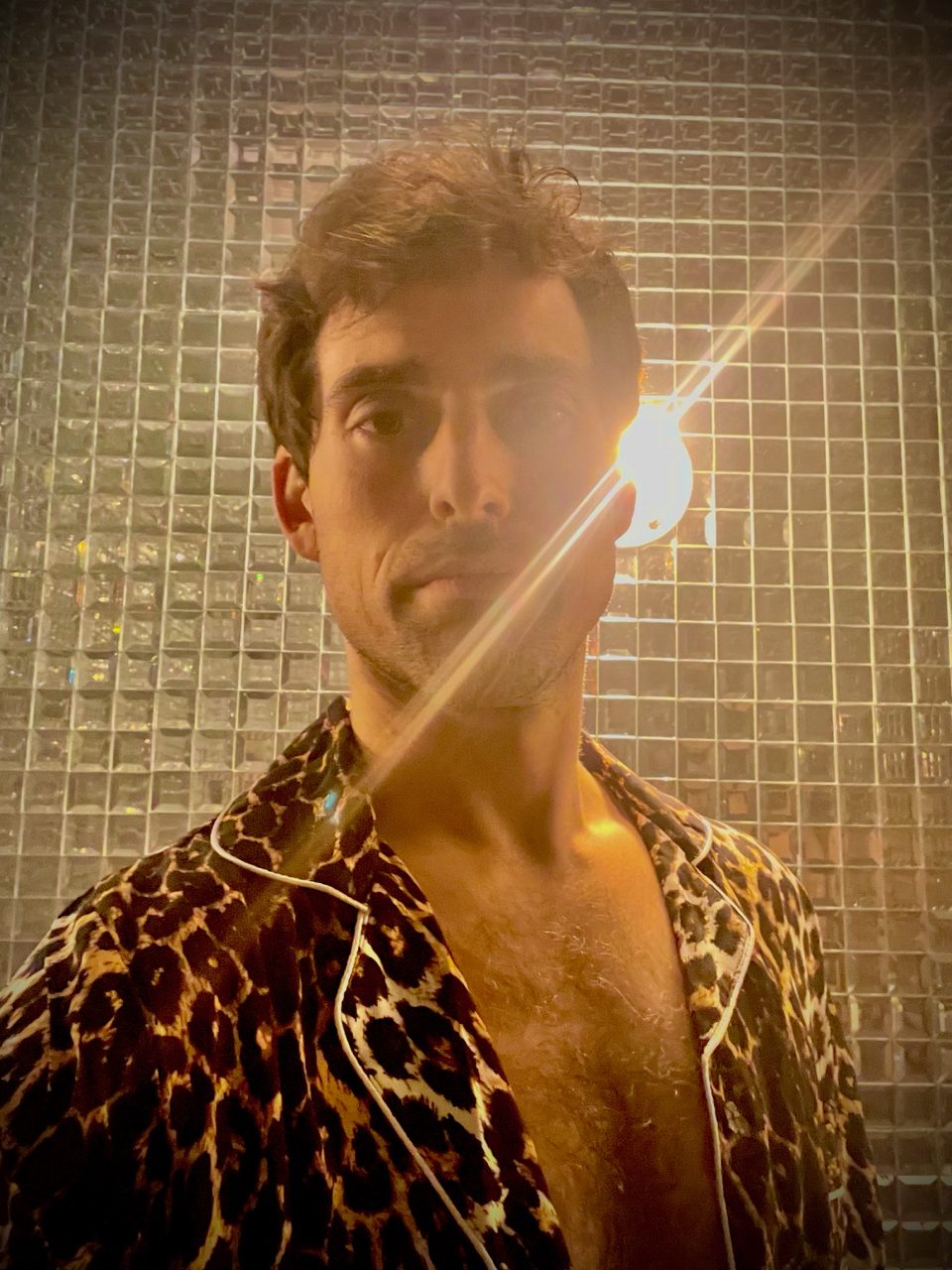 Aaron in leopard pajamas against a mirrored tile wall, lens flare across his face