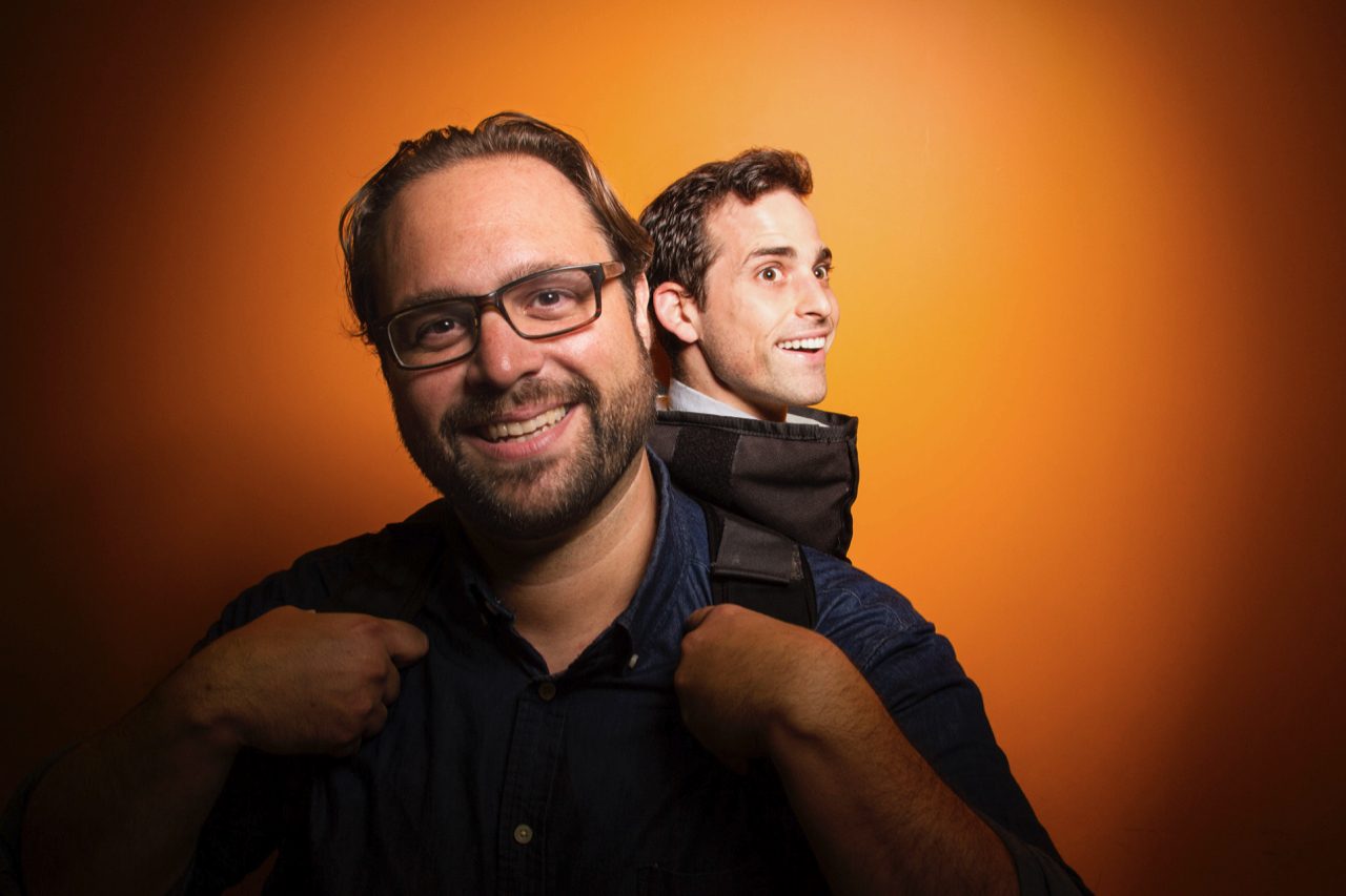 Aaron peeking over a collaborator's shoulder against an orange backdrop
