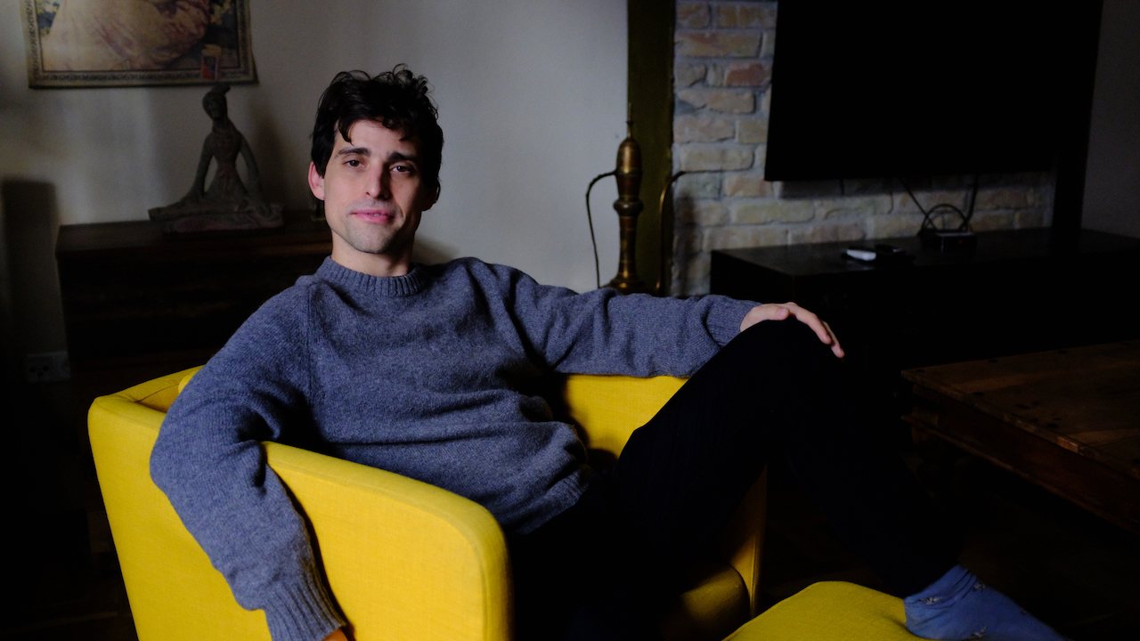Aaron lounging in a yellow armchair in a dim living room